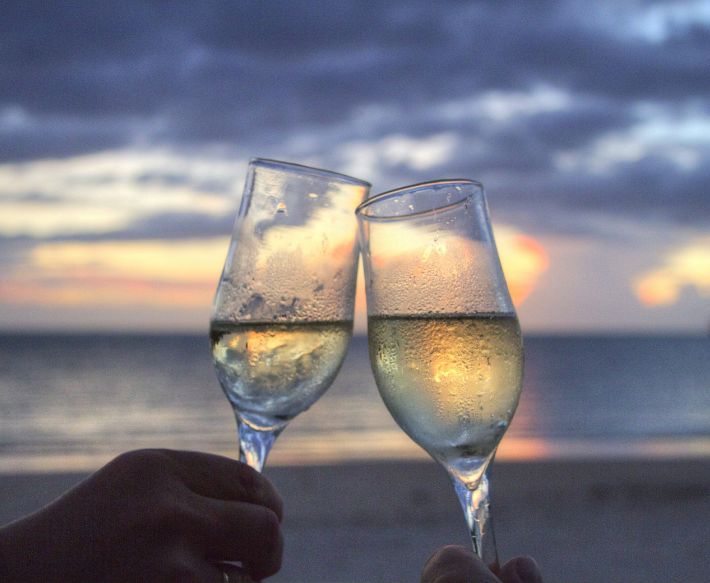 Two people clinking glasses of champagne on beach in front of ocean at Ocean City Fontainebleau Resort in Ocean City, MD