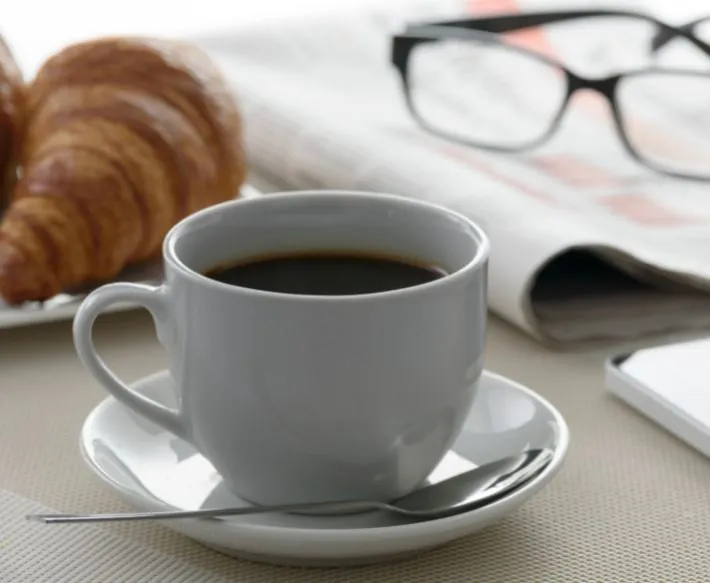 Cup of coffee on white plate next to croissant, newspaper and glasses at Ocean City Fontainebleau Resort in Ocean City, MD